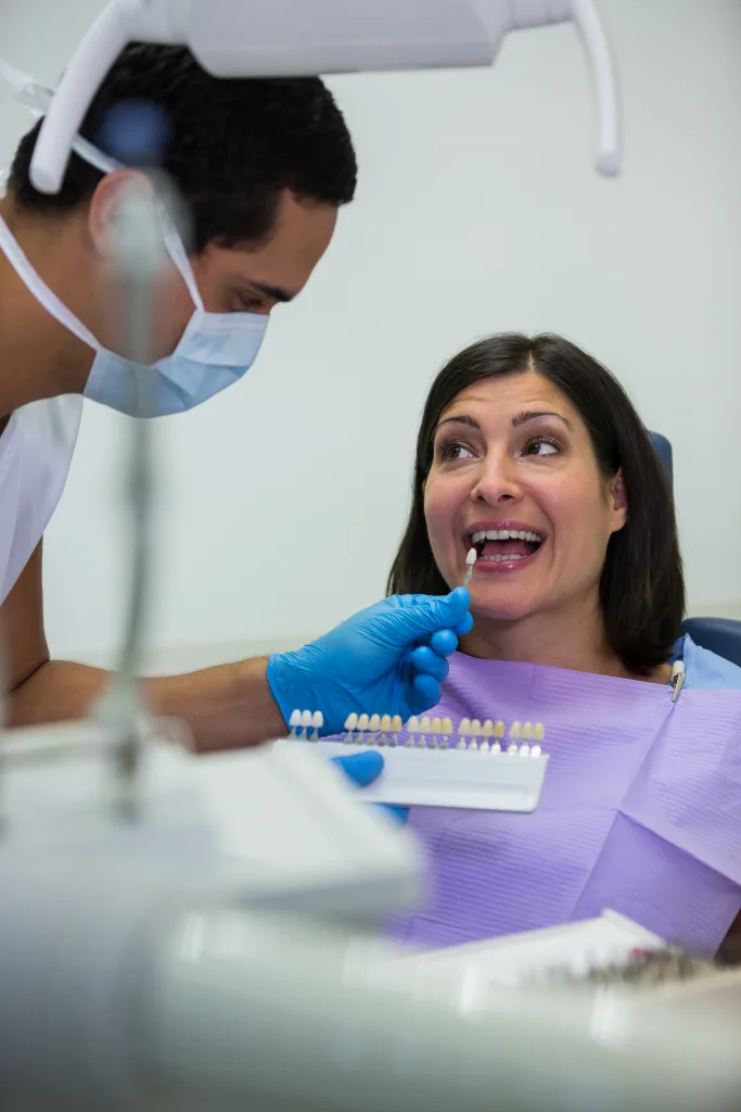 Dentist examining female patient with teeth shades at dental clinic